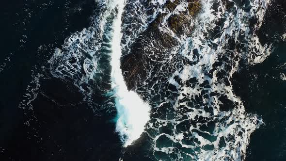 Sea waves with sea foam splash on a large boulder. Perpendicular aerial view.