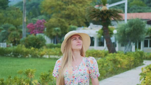Graceful Woman in Summer Hat Visiting Park with Exotic Plants