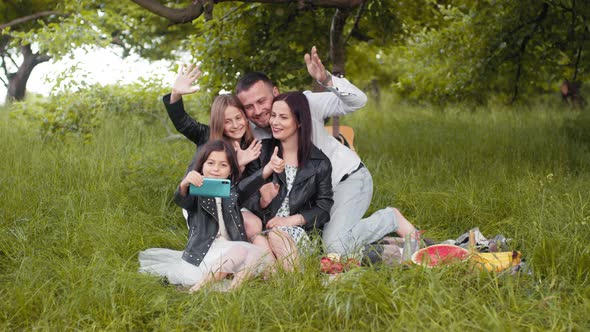 Cheerful Parents and Their Cute Daughters Sitting Together on Green Grass and alt