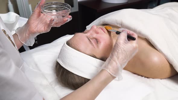 The Cosmetologist Applies a Transparent Mask with a Brush To the Client's Face