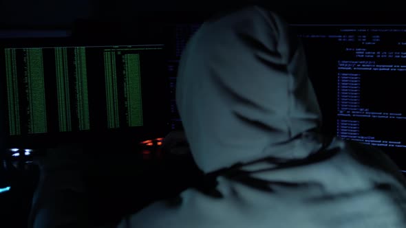 The Man In The Hood Is Typing On The Keyboard, Hacker Is Programming While Looking At The Monitor alt
