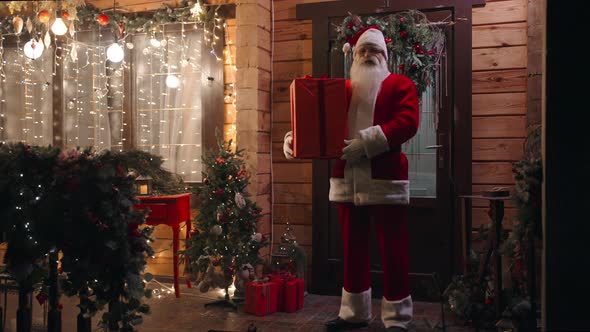 Zoom Camera Santa Claus Stands Outside the House Outdoors in Winter with a Gift and Looks Into the alt