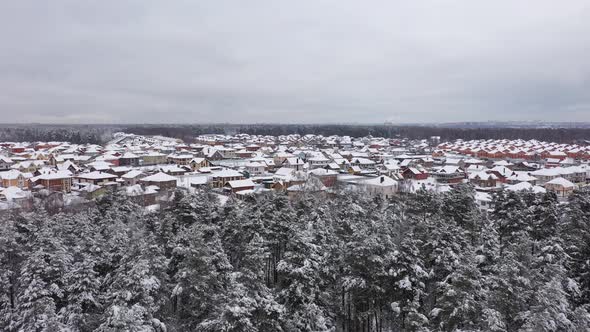 Drone Flying Over Forest Towards Cottage Village Covered By Snow