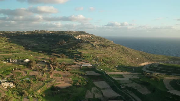 AERIAL: Flying Above Green Farm Lands near Coastline of Malta in Winter During Golden Hour