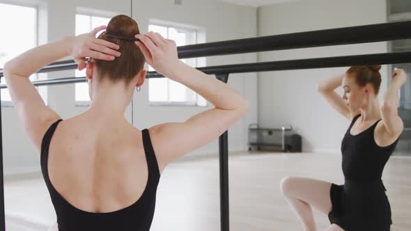 Caucasian female ballet dancer preparing for dance class in a bright studio alt