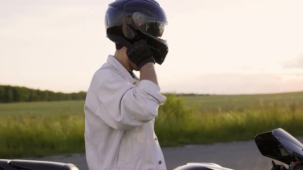 Motorciclist Sits on Motorcycle and Puts Helmet on Head