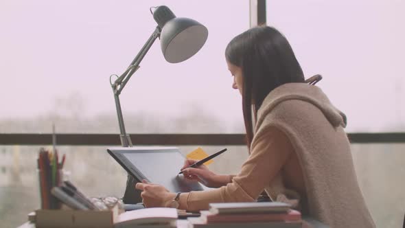 Young Woman Sitting at Her Desk She's Drawing Writing and Using Pen with Digital Tablet Computer alt
