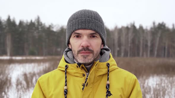 A man in a yellow jacket looks directly at the camera while standing on the field alt