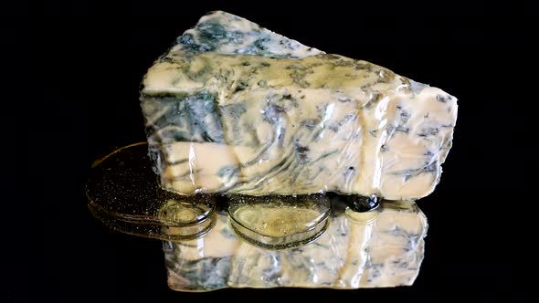 Drops of honey flowing down from the Dorblu cheese on a mirrored black background. alt