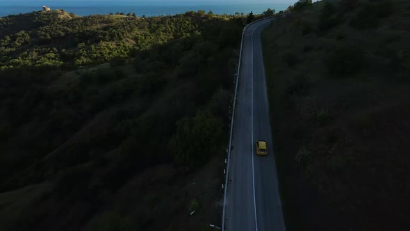 Aerial View of a Car Driving Along a Winding Mountain Road Through a Valley alt