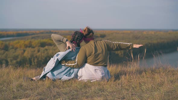Lesbian Exhilarated Couple Sits on River Bank in Autumn alt
