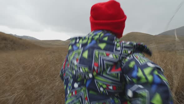 Boy Runs on High Dry Grass Among Hills on a Cloudy Day