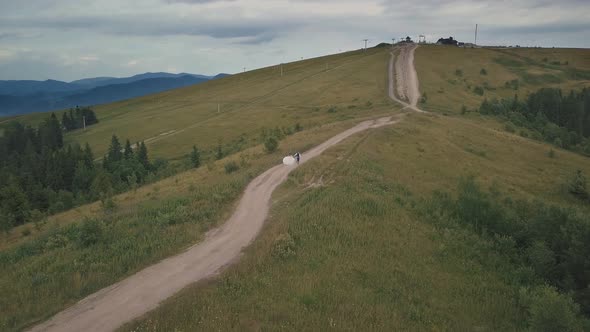 The Groom Runs with Bride on a Mountain Hills. Aerial Drone Shot alt