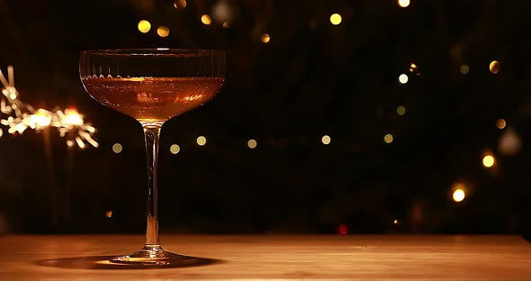 one Glass Of Champagne And Dark Background With Festive Gold Lights And New Year Sparkler.