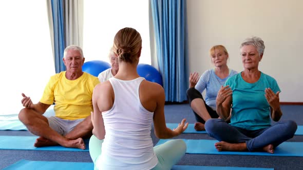 Trainer assisting senior citizens in practicing yoga alt