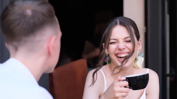 Beautiful and Smiling Bride Drinks a Cup of Coffee and Talks to the Groom alt