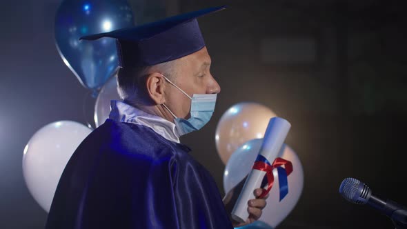 Male Rector Wearing Medical Mask Wearing an Academic Cap and Mantle Conducts Graduation Ceremony Via alt