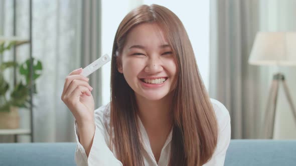 Happy Young Asian Woman Holding Pregnancy Test And Warmly Smiles To Camera alt