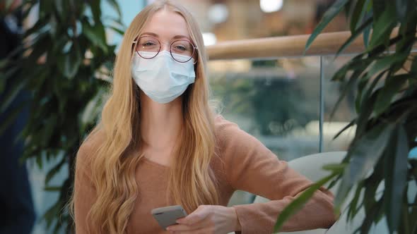 Caucasian Successful Business Woman Girl in Medical Mask Indoors with Mobile Phone Success Online alt