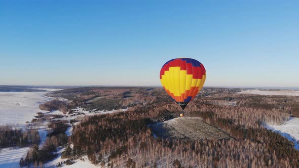 Aerial Shot of the People Fly on a Big Bright Balloon Over the Winter Forest.