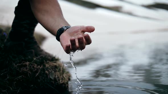 Man picks up water in his hand from a mountain lake with crystal clear water alt