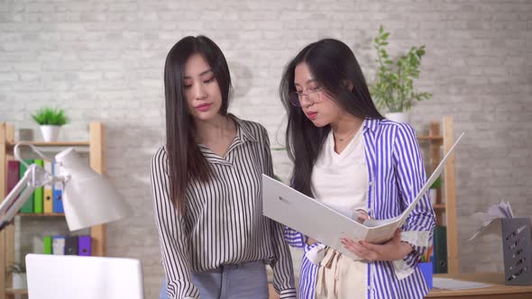Two Young Asian Girls Office Workers Discuss Documents alt