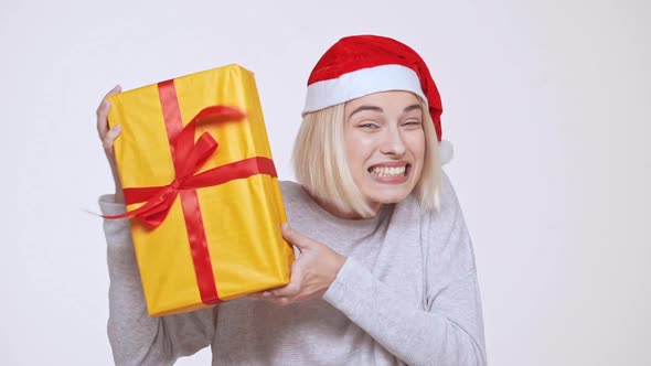 Young Beautiful Excited Blonde Girl in Christmas Hat Holding Gift Box White Background Slow Motion alt
