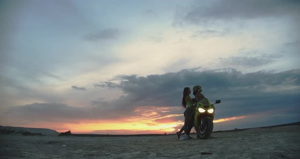 Couple Embracing Near Motorbike on Beach at Sunset