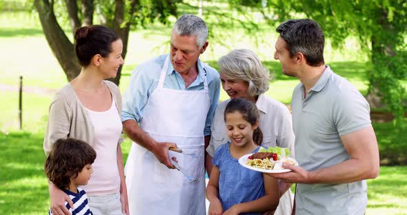 Happy Grandfather Serving Burgers at Family Barbecue in the Park alt