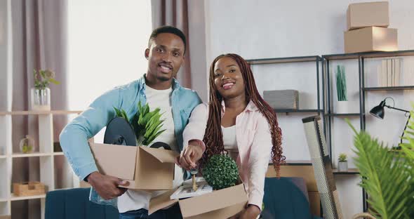 African American Couple Holding Carton Boxes with Flowers and Looking at Camera alt