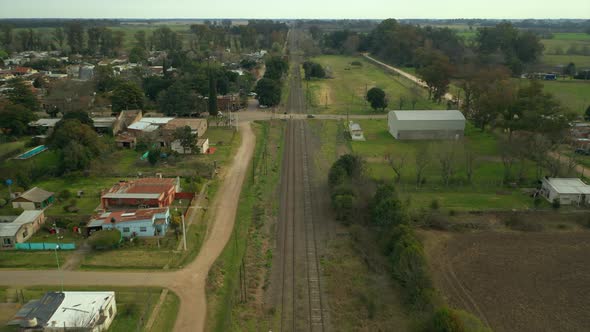 Aerial: slowly moving forward over railway tracks, afternoon rural town, countryside, Argentina. alt