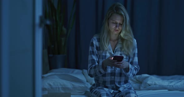 Young Beautiful Girl Sitting on the Bed with Her Phone