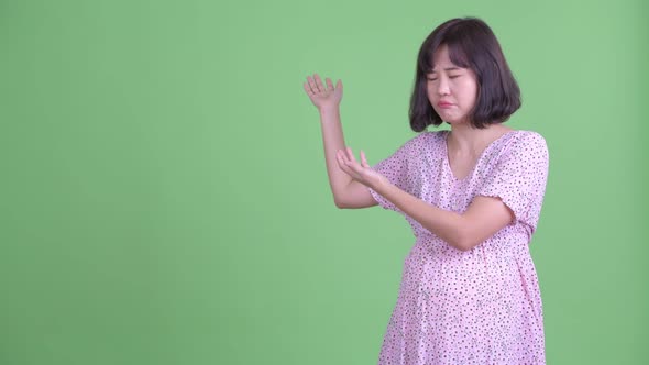 Stressed Asian Pregnant Woman Showing To the Back and Giving Thumbs Down alt