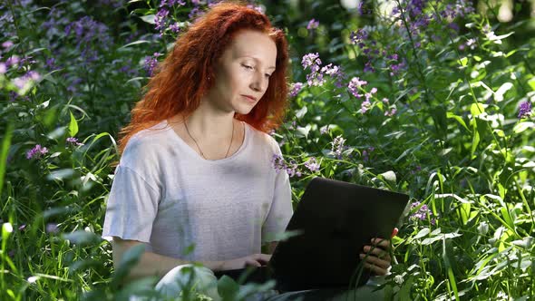 Redhead Woman Work on Laptop Computer Among Flowers in a City Park