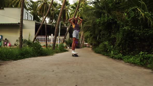 Beautiful and cute young caucasian girl riding the skateboard on the road between the palm trees and alt