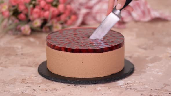 Cutting chocolate mousse cake with cherries jelly.	