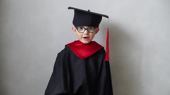Smiling Little Boy Showing His First Diploma in Graduation Gown