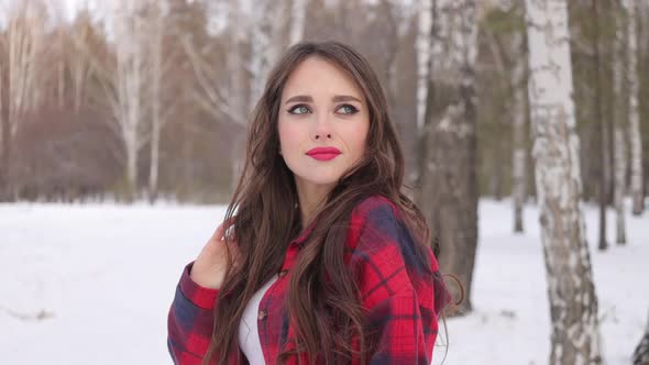 Young Woman with Wavy Hair Standing and Touching Face in Winter Forest