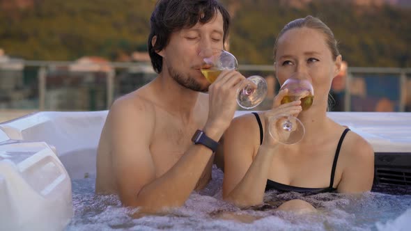 A Young Man and Woman are Relaxing in the Hot Tub on a Rooftop with a View on Mountains During alt