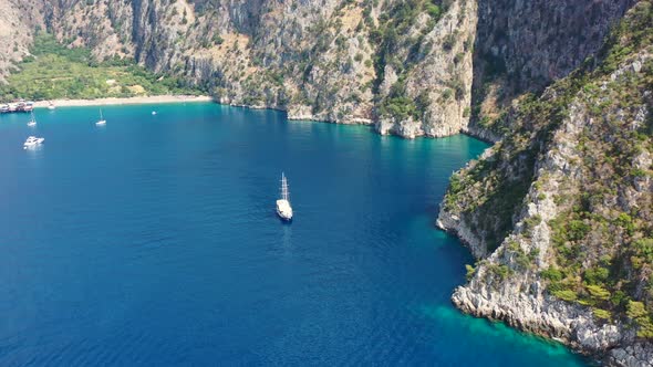 aerial drone approaching a large sailboat docked in the bay of Butterfly Valley surrounded by turquo alt