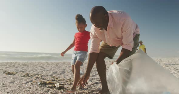 Senior african american couple with grandchildren segregating waste on sunny beach alt