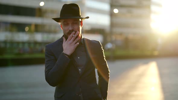 Portrait of a Smoking Bearded and Mustachioed Man in a Hat and Jacket in the Contrasting Sunlight alt