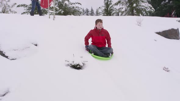 Boy sledding down snow covered hill in winter