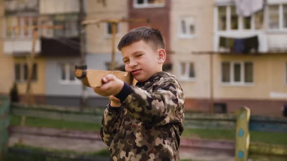 Urainian Boy in Camouflage with Wooden Toy Gun Aims Forward