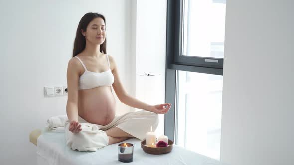 Pregnant Asian Woman Relax Doing Yoga Sitting in Lotus Position in Spa Cabinet