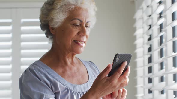 African american senior woman using smartphone and looking out of the window at home alt