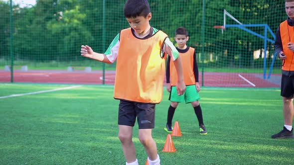 Teen Boys in Football Uniforms which Doing Running Exercises with Obstacles with Ball alt