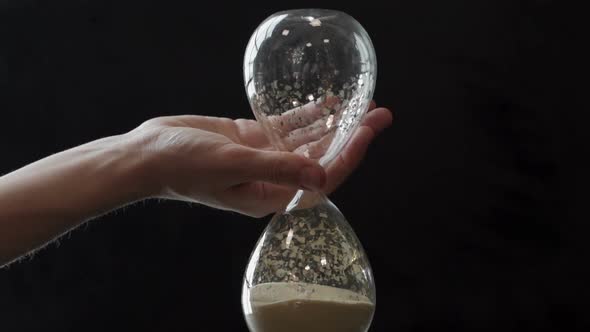 Vintage Glass Hourglass Inverted By a Woman's Hand on a Black Background alt