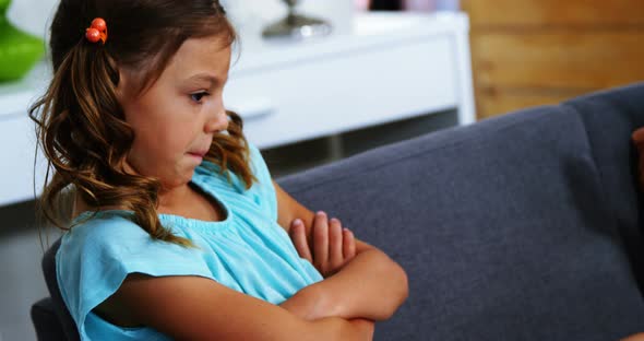 Sad girl sitting with arms crossed in living room alt