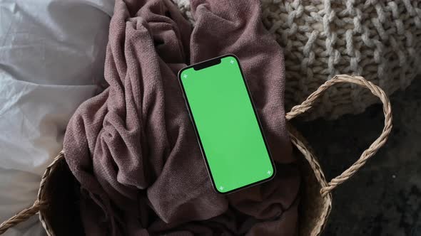 Modern smartphone laying on cozy grey blanket at home with green screen chromakey